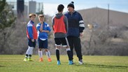 football coach talking to one male player whilst two others watch from behind
