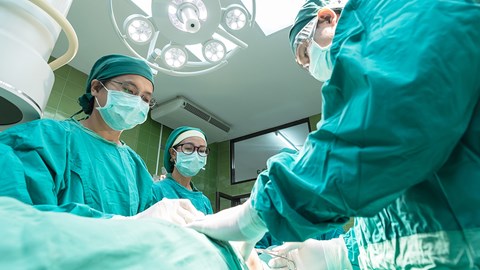 three doctors in a theatre conducting surgery 
