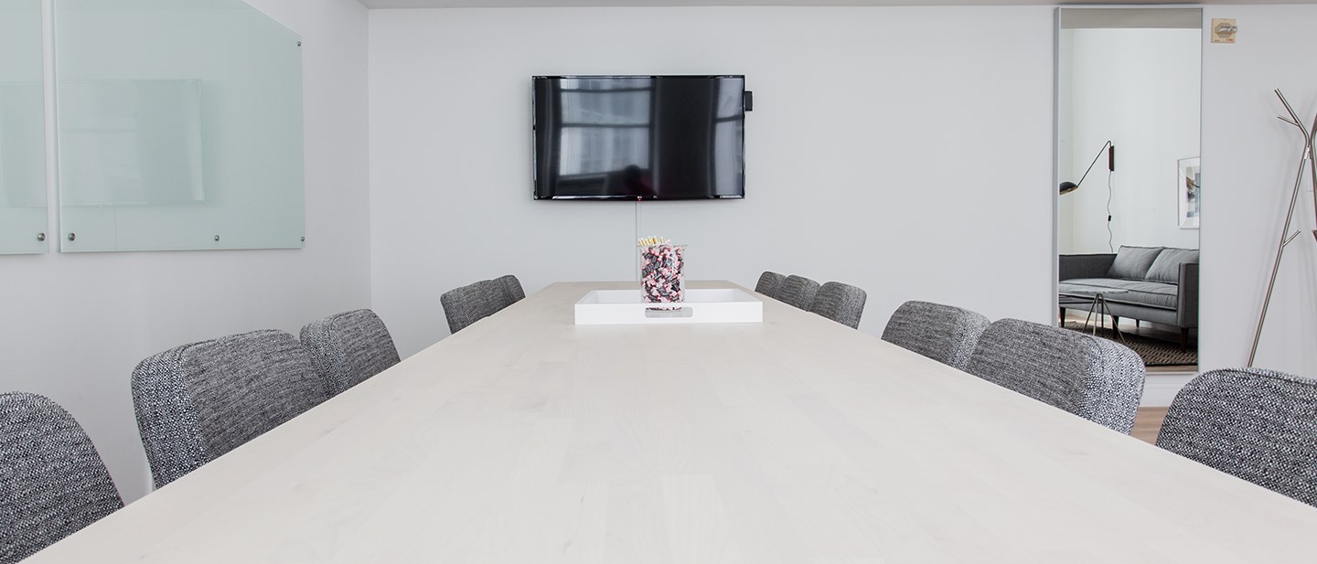Empty board room with a white table, black chairs and a TV screen