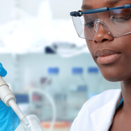 A student is wearing lab coat ,safety glasses and safety gloves experimenting with lab equipment in the lab.