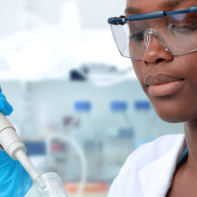 A student is wearing lab coat ,safety glasses and safety gloves experimenting with lab equipment in the lab.