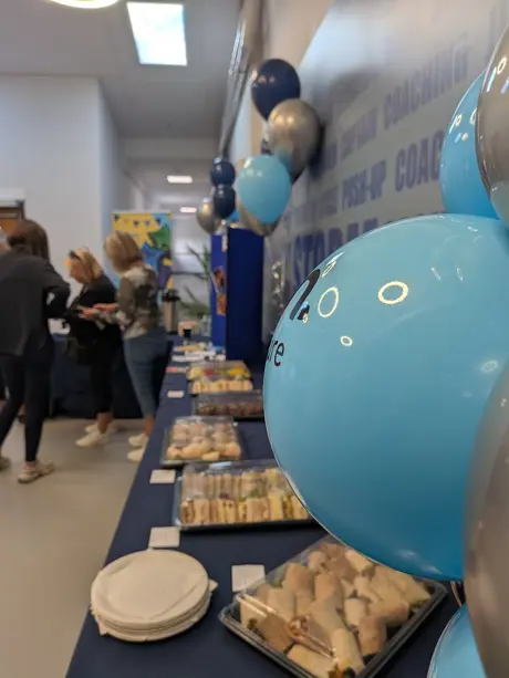 picture of blue balloon in main frame, with party taking place in background with table of food 