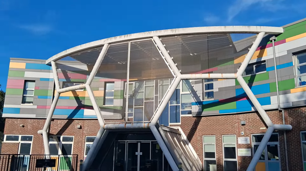 exterior image of the XTEND Digital campus. A brick building on the lower floor, with multi-coloured panels of cladding on the upper floor, with a white hexagonal metal frame to cover the main entrance