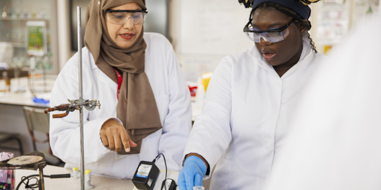 A female student and a female teacher in lab coats doing a science experiment.