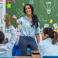 A teacher standing in the class with early years students wearing a blue shirt .