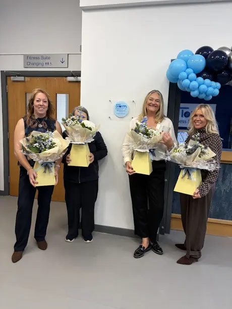 4 women posing in a line looking into the camera each holding a bunch of blue and white flowers