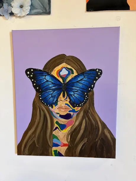 A photograph of a hand painted portrait of a girl with long brown hair on a purple background. The girl has a blue butterfly covering much of her face.