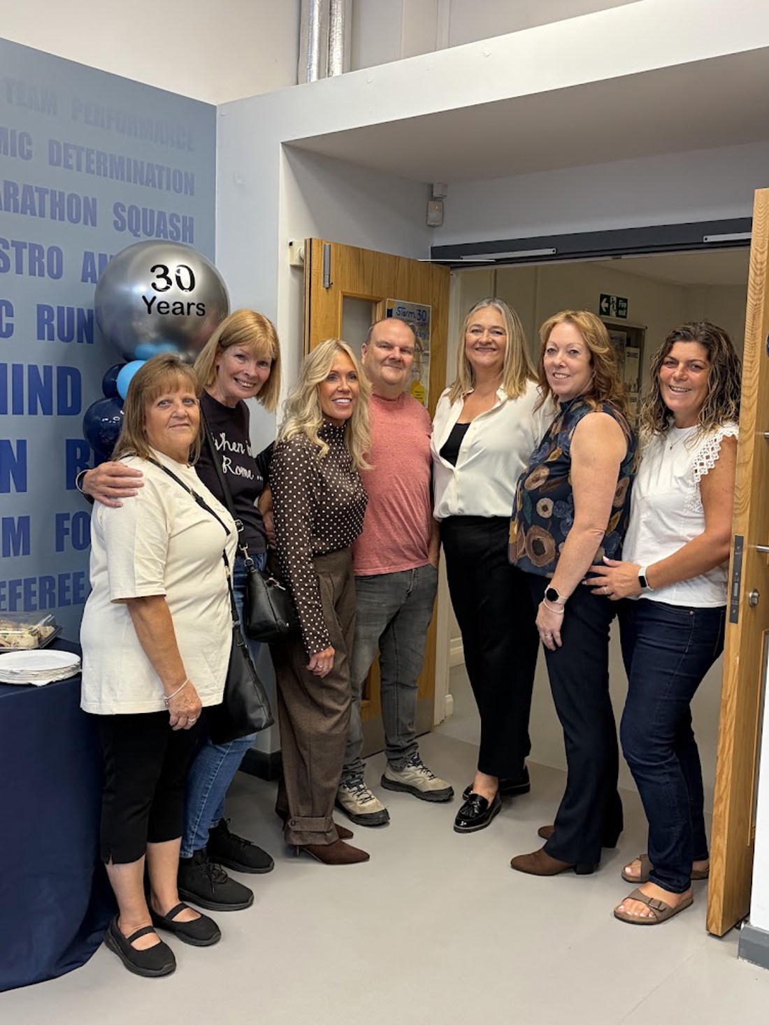 group picture of 7 people (6 women with 1 man in the middle) all smiling looking into the camera